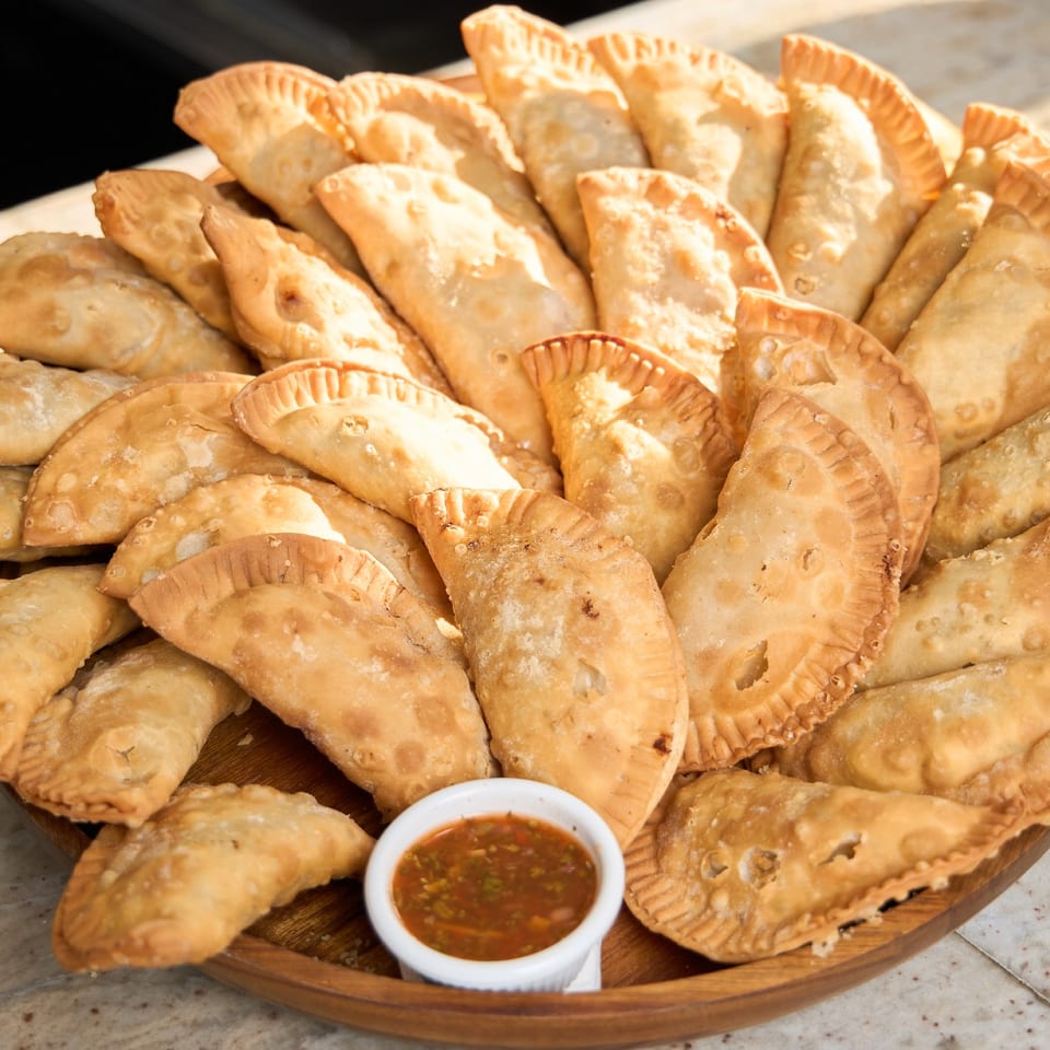 Wooden platter of golden fried empanadas with a side of red dipping sauce.