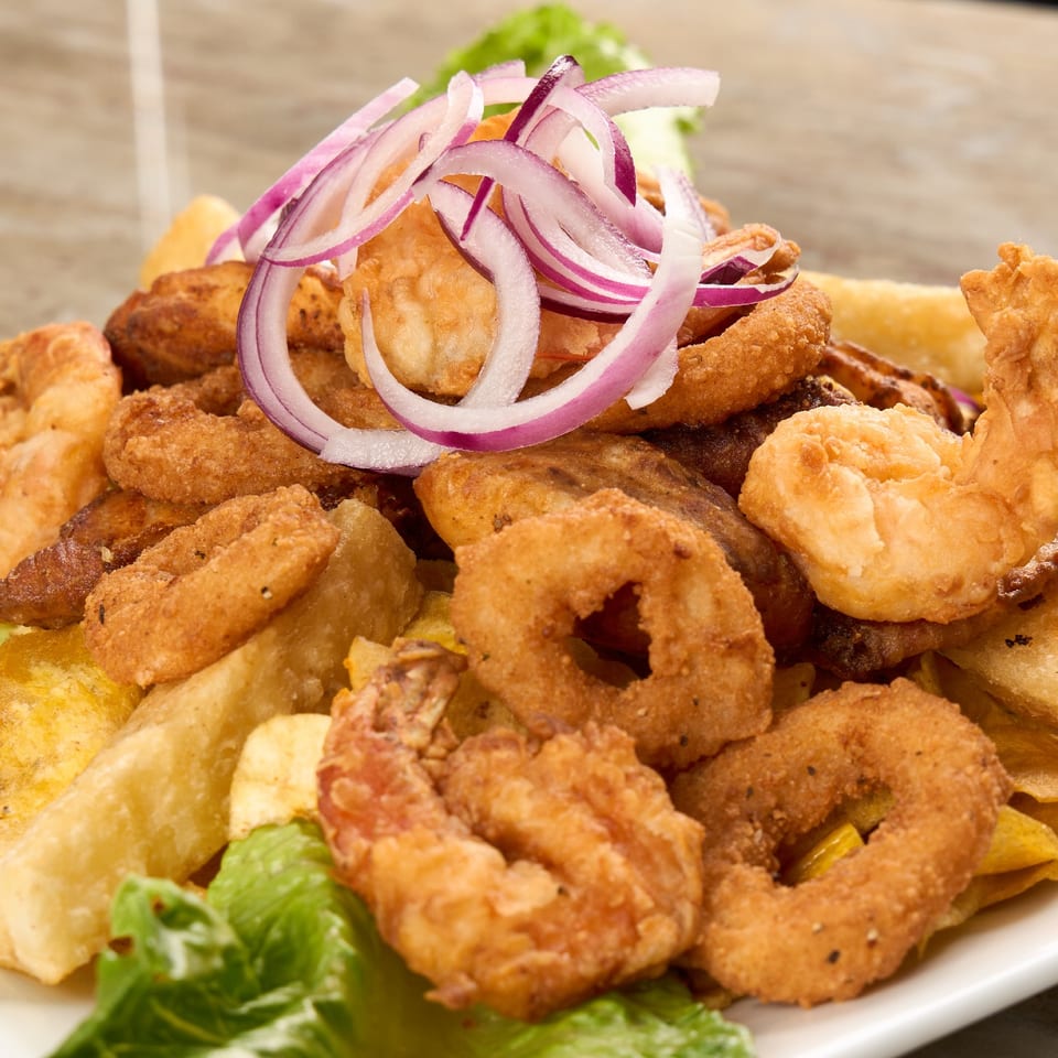 Fried seafood platter with shrimp, calamari rings, and plantain chips topped with red onion.