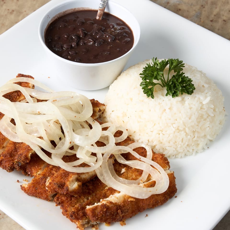 Breaded chicken cutlet topped with onions, served with white rice and black beans.